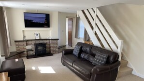 Ein Wohnzimmer mit Kamin, einer Couch, einem Fernseher und einer Treppe.