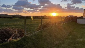 Ländliche Landschaft mit Sonnenuntergang, offenen Feldern und einem Haus in der Ferne.