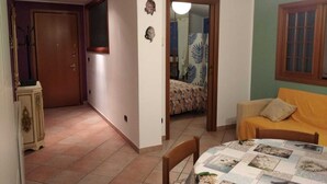 Quarto com cama, sofá, mesa de jantar com colcha e porta que dá para outro espaço.