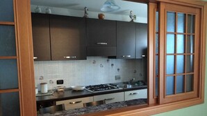 Uma cozinha com armários escuros, um fogão a gás e uma janela com painéis de vidro jateado.