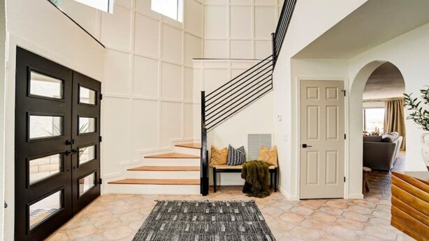 A spacious foyer with a staircase, a black door, and a bench with cushions. - Best Luxury Riverfront Home w/ Private Pool & Dock (Bullhead City)