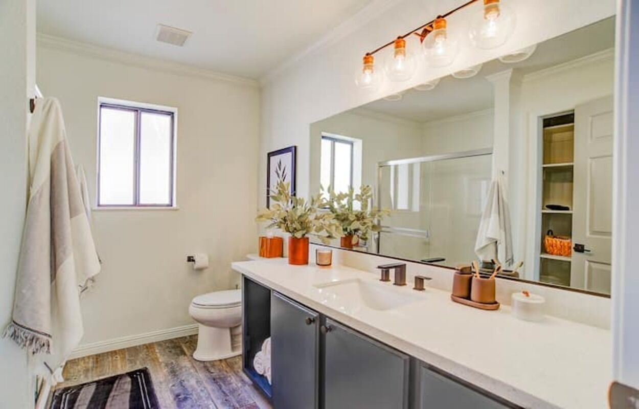 A bathroom with a white sink, mirror, and a window. There are towels hanging on the wall and a plant on the counter.