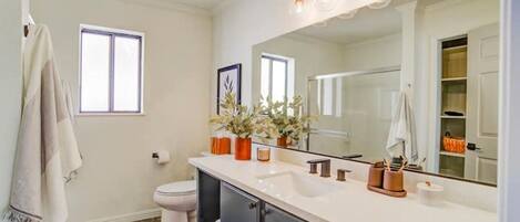 A bathroom with a white sink, mirror, and a window. There are towels hanging on the wall and a plant on the counter.