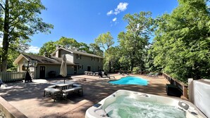 Un patio trasero con un jacuzzi, una piscina y una casa con terraza y mobiliario exterior.