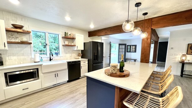 Una cocina moderna con armarios blancos, una isla grande y una zona de comedor con sillas de mimbre.