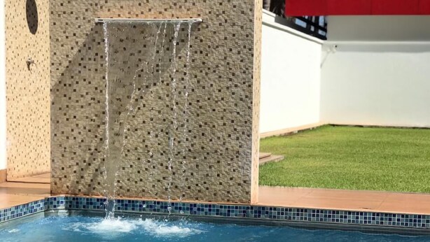 Una piscina amb vora de rajola, una pila de tovalloles blanques i una paret amb un relleu decoratiu.