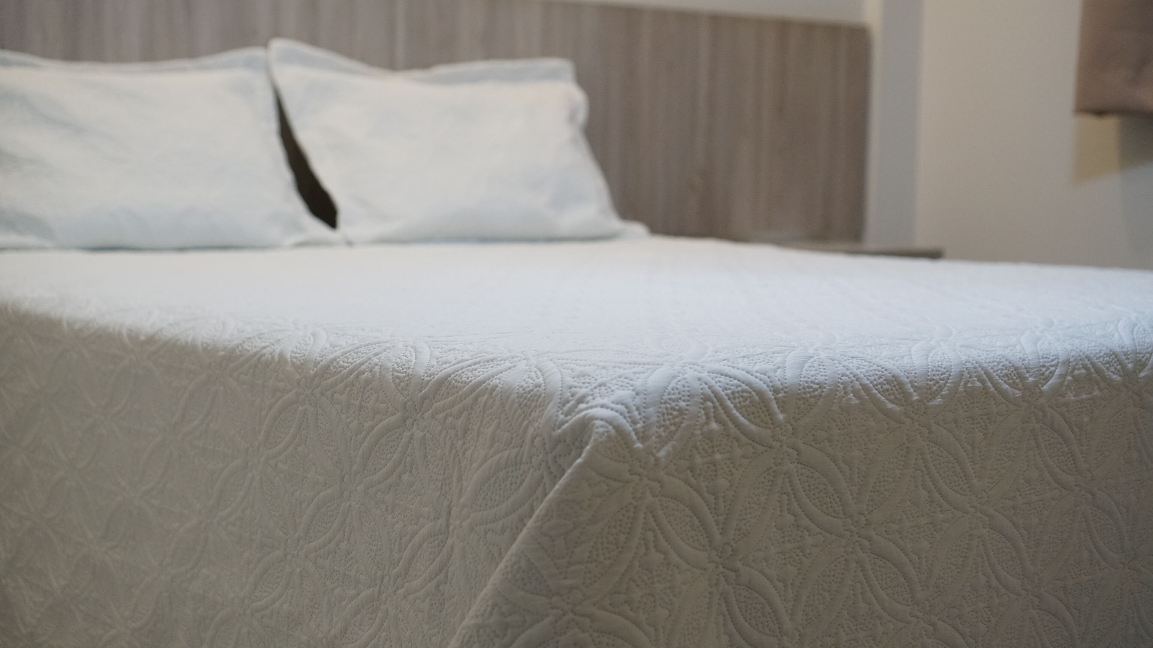 Cama bem arrumada com um espesso cobre leito branco e duas almofadas.