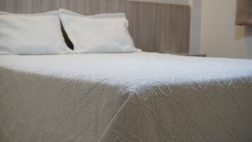 Cama bem arrumada com um espesso cobre leito branco e duas almofadas.