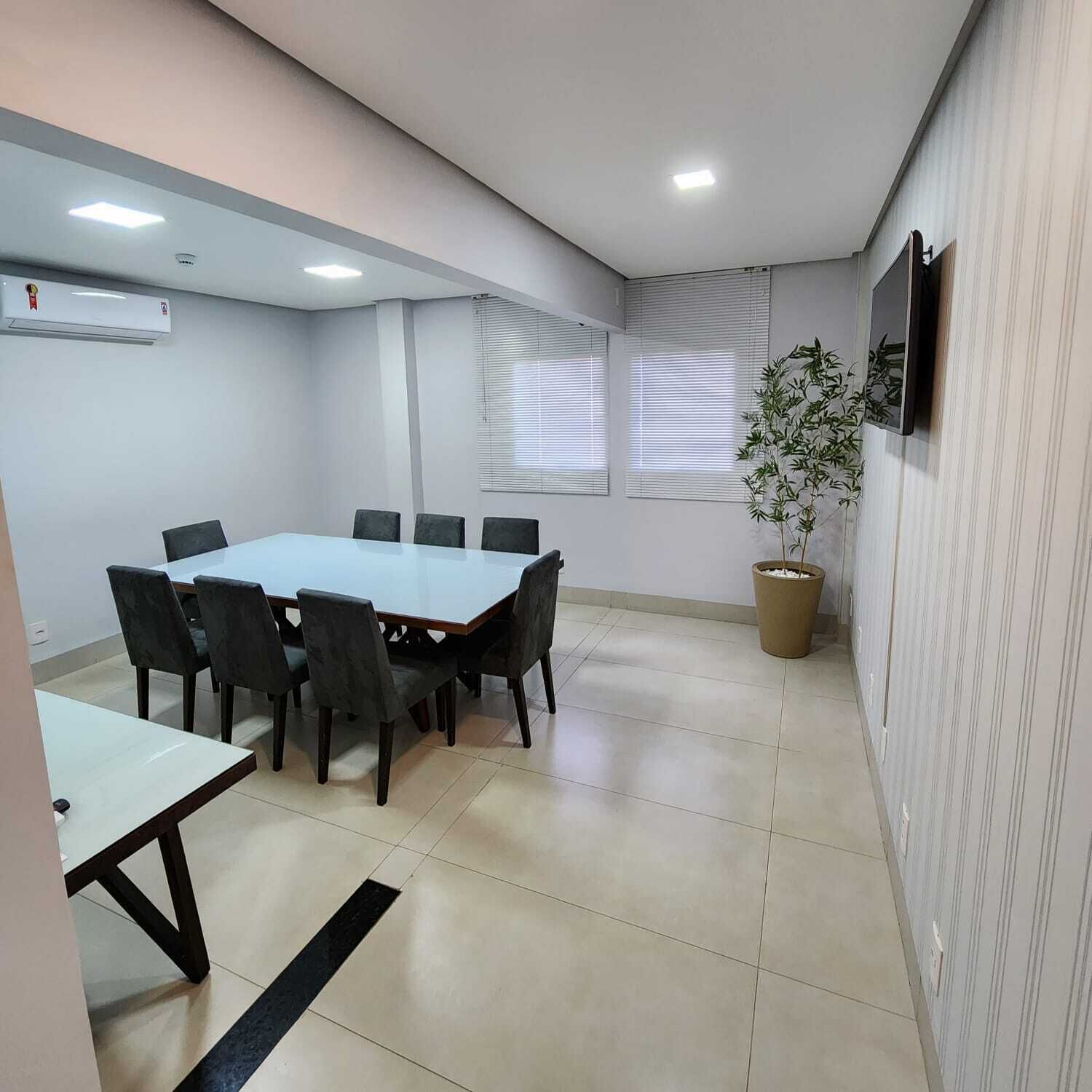 A conference room with a rectangular table, six chairs, a potted plant, and a television on the wall.
