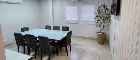 A conference room with a rectangular table, six chairs, a potted plant, and a television on the wall.