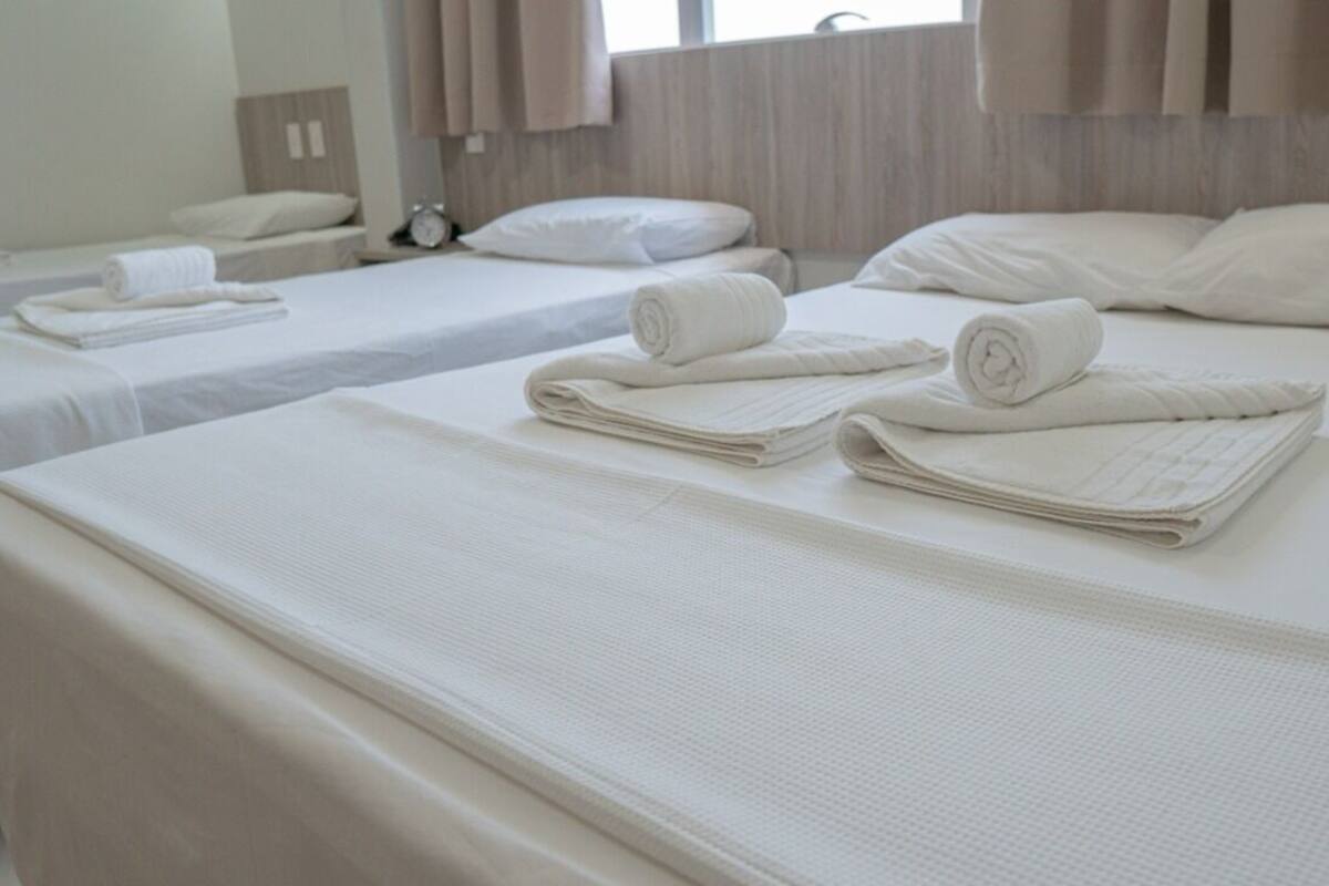 A hotel room with three neatly made beds, each with rolled towels and pillows.