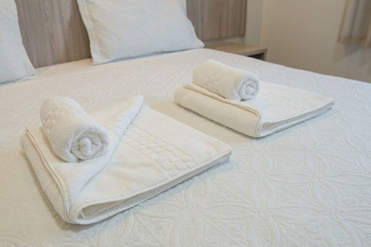 A neatly made bed with two rolled towels and a pillow.