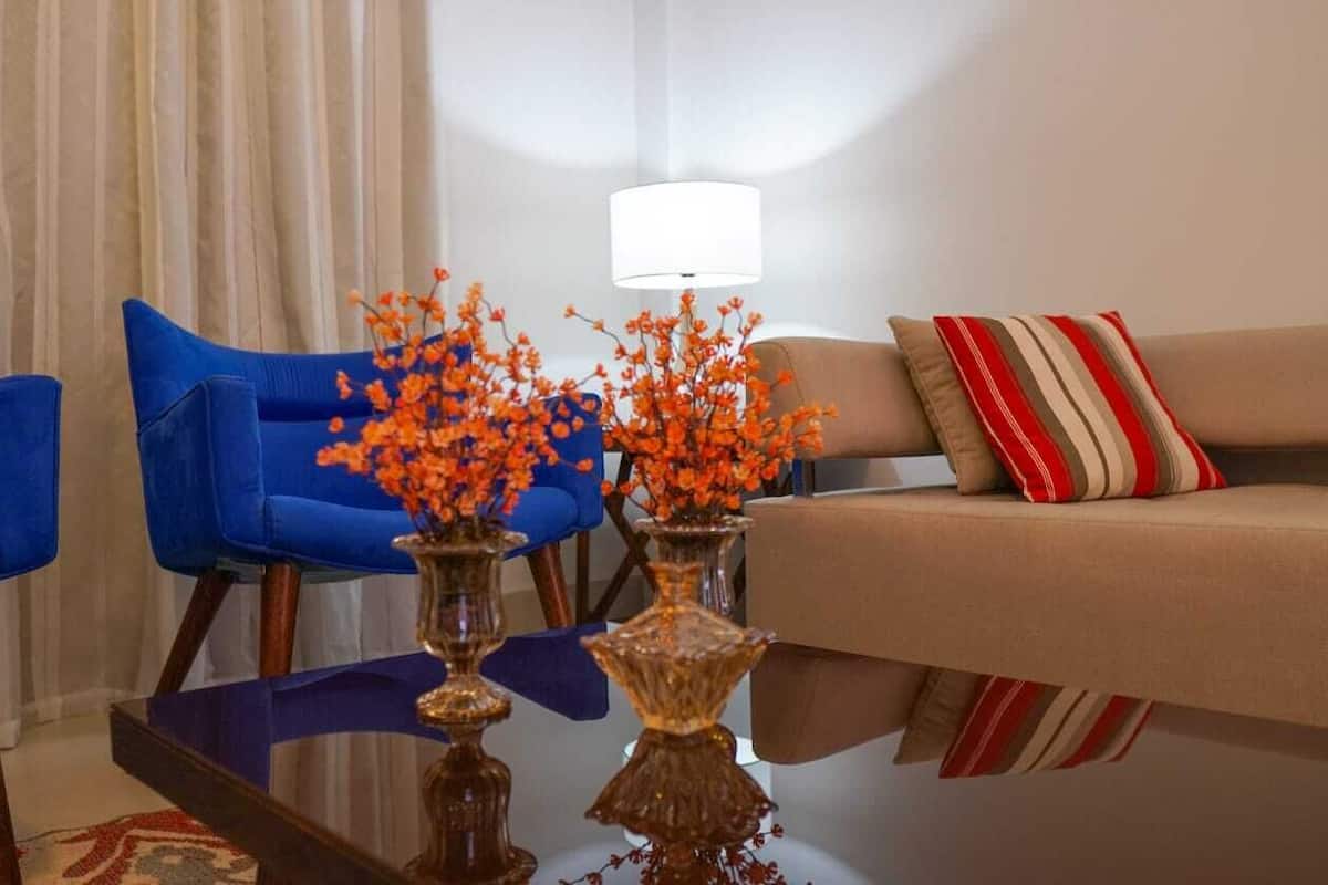 A living room with a beige sofa, a blue armchair, and two vases with orange flowers.