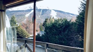 Ein Zimmer mit großem Fenster und Blick auf eine verschneite Berglandschaft sowie einen bewaldeten Bereich.