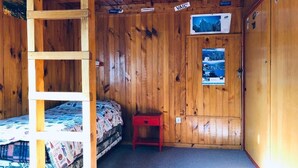 Ein Zimmer in einer Holzhütte mit einem Stockbett, einem kleinen roten Tisch und einer Tür mit einem Plakat.