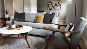 Una sala moderna con un sofá gris, una mesa de centro de madera y un sillón gris.
