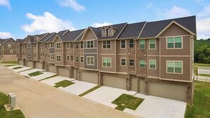 Una hilera de casas adosadas con garajes incorporados, un camino de entrada pavimentado y un césped.