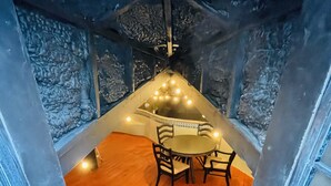 Une pièce en forme d’igloo de glace, avec un plancher en bois, une table ronde entourée de chaises et des guirlandes lumineuses suspendues au plafond.
