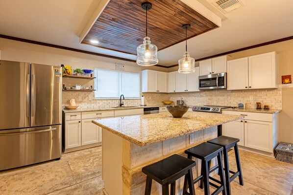 Una cocina moderna con una isla grande, electrodomésticos de acero inoxidable e iluminación colgante.