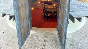 Une structure ouverte comprenant une table et des chaises à l’intérieur, un luminaire suspendu et un mur en pierre.