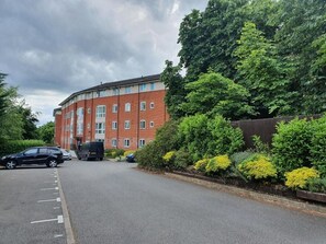 A multi-story red brick building with a curved facade, a parking lot with cars, and lush greenery. - 2 Bed Apt Near Hatfield Station w/ Free Parking (Hatfield)