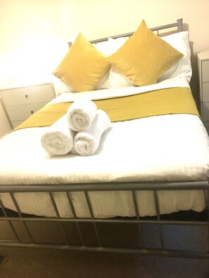 A bed with white bedding, two yellow pillows, and three rolled white towels. - 2 Bed Apt Near Hatfield Station w/ Free Parking (Hatfield)
