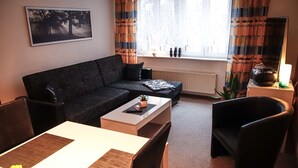 A living room with a sofa, a coffee table, a dining table with chairs, a window with curtains, and a wall-mounted picture.