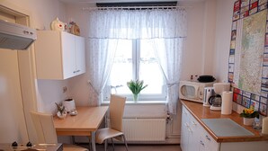 A compact kitchen with a dining table, chairs, a microwave, a kettle, and a radiator.