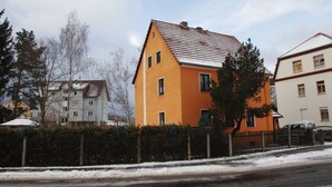 A residential building with a sloped roof, a fenced yard, and a snow-covered ground.