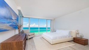 A modern bedroom with a large window, a bed, a desk, and a nightstand. - Oceanfront Private Condo at 1 Hotel & Homes-1019 (Miami Beach)