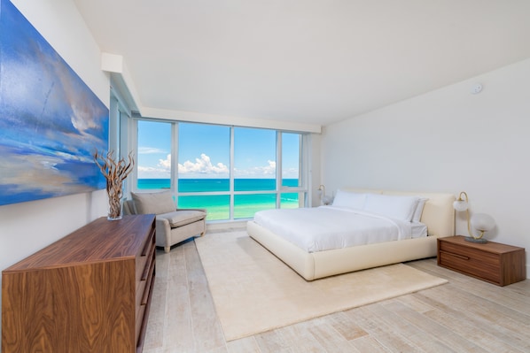 Un dormitorio moderno con una ventana grande, una cama, un escritorio y vista al océano.