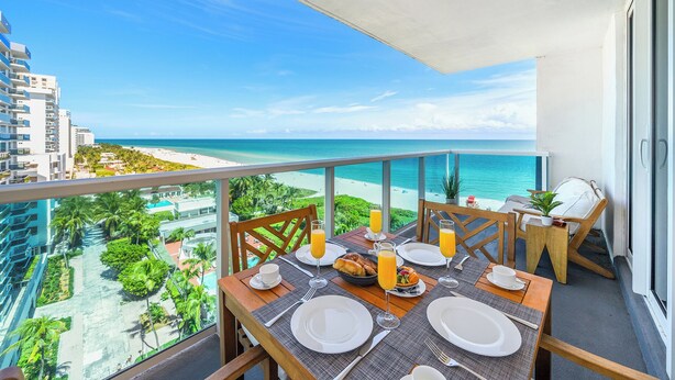 A balcony with a table set for breakfast, overlooking a beach and ocean. - Oceanfront Private Condo at 1 Hotel & Homes-1019 (Miami Beach)