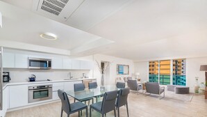 A modern kitchen with stainless steel appliances, a glass dining table with chairs, and a view of a swimming pool through large windows. - Oceanfront Private Condo at 1 Hotel & Homes-1019 (Miami Beach)