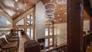 Un interior de madera con una zona de bar, chimenea de piedra y grandes ventanales.