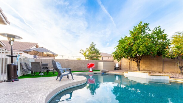 A backyard with a swimming pool, patio furniture, and a basketball hoop.