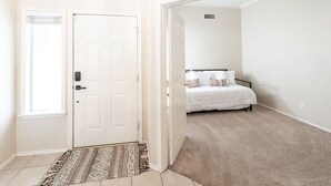 A bedroom with a white door, a patterned rug, and a bed with white bedding.