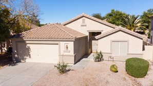 A single-story house with a garage, a small porch, and a landscaped front yard with shrubs and a palm tree.
