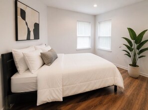 Een slaapkamer met een bed, een kamerplant en een schilderij aan de muur.