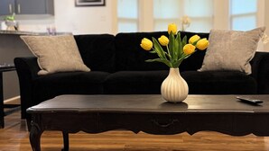 Een moderne woonkamer met een donker houten salontafel, een zwarte bank en een vaas met gele tulpen.
