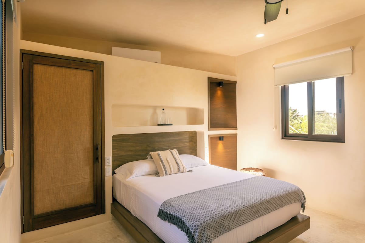 Un dormitorio con cama, una puerta de madera, una ventana y una estantería con una lámpara.