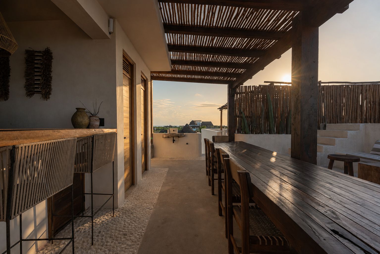 A covered outdoor seating area with a wooden table and chairs, a view of the landscape, and a pergola structure.