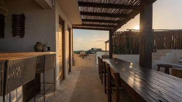 A covered outdoor seating area with a wooden table and chairs, a view of the landscape, and a pergola structure.