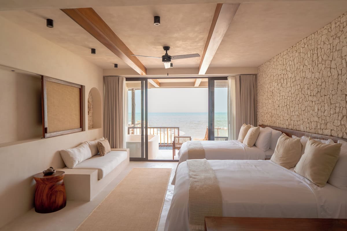 Habitación de hotel con dos camas, un balcón con vista al mar y un ventilador de techo.