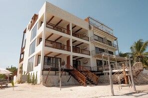 A multi-story building with balconies, a staircase, and a sandy ground. - Hotel Boutique Casa Muuch Holbox (Isla Holbox)