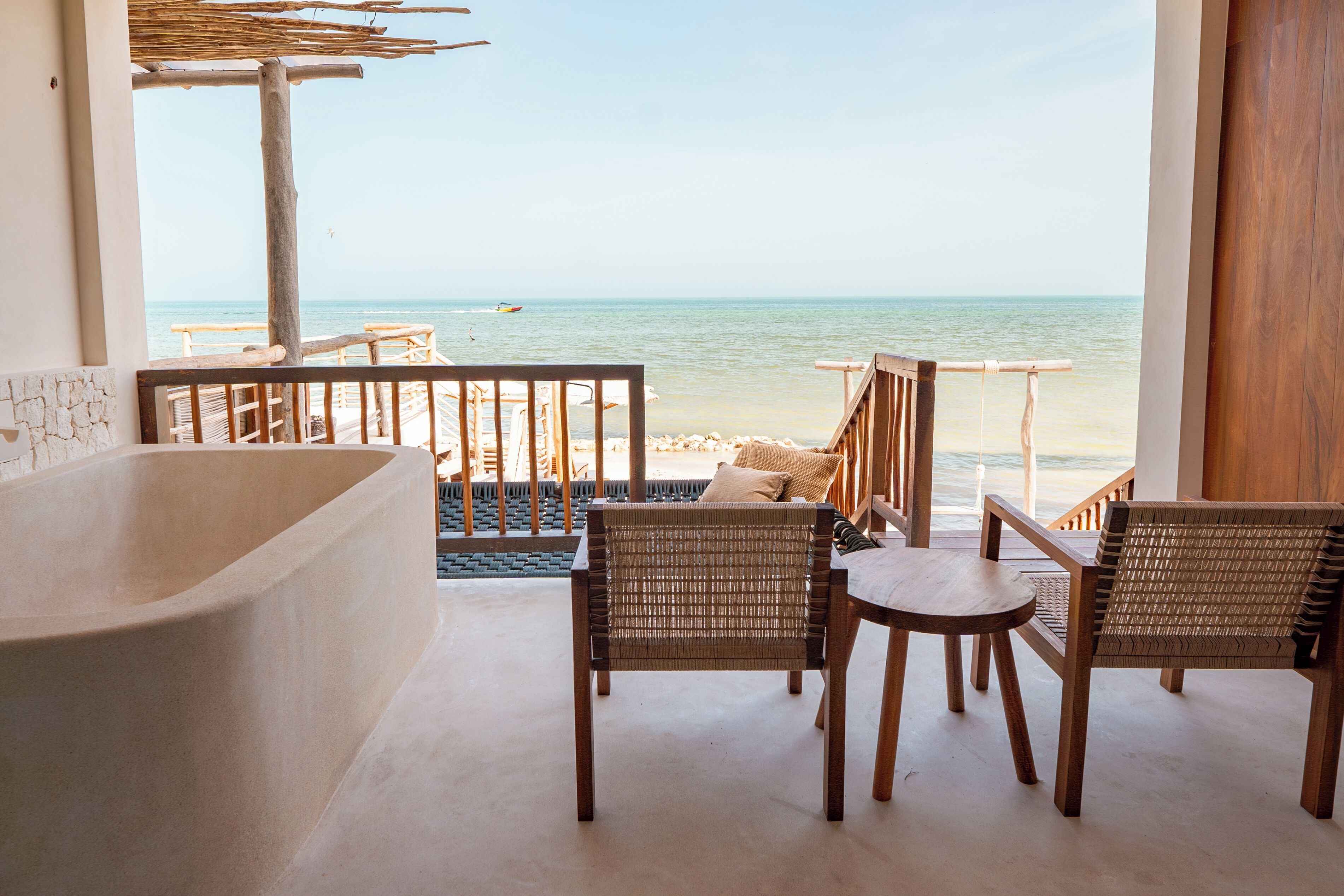 Un balcón con vista al mar, muebles de madera y una bañera.