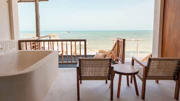 Un balcón con vista al mar, muebles de madera y una bañera.