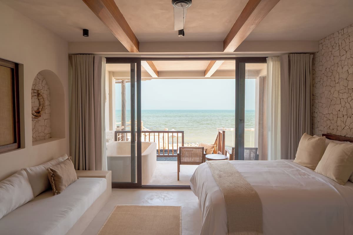 Una habitación de hotel con una cama grande, un sofá, un balcón con vista al mar y un ventilador de techo.
