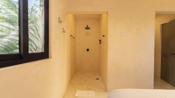 A narrow shower room with a window, a towel on the floor, and a door leading to another room.