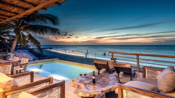 A poolside area with wooden furniture and a view of the beach at sunset. - Hotel Boutique Casa Muuch Holbox (Isla Holbox)