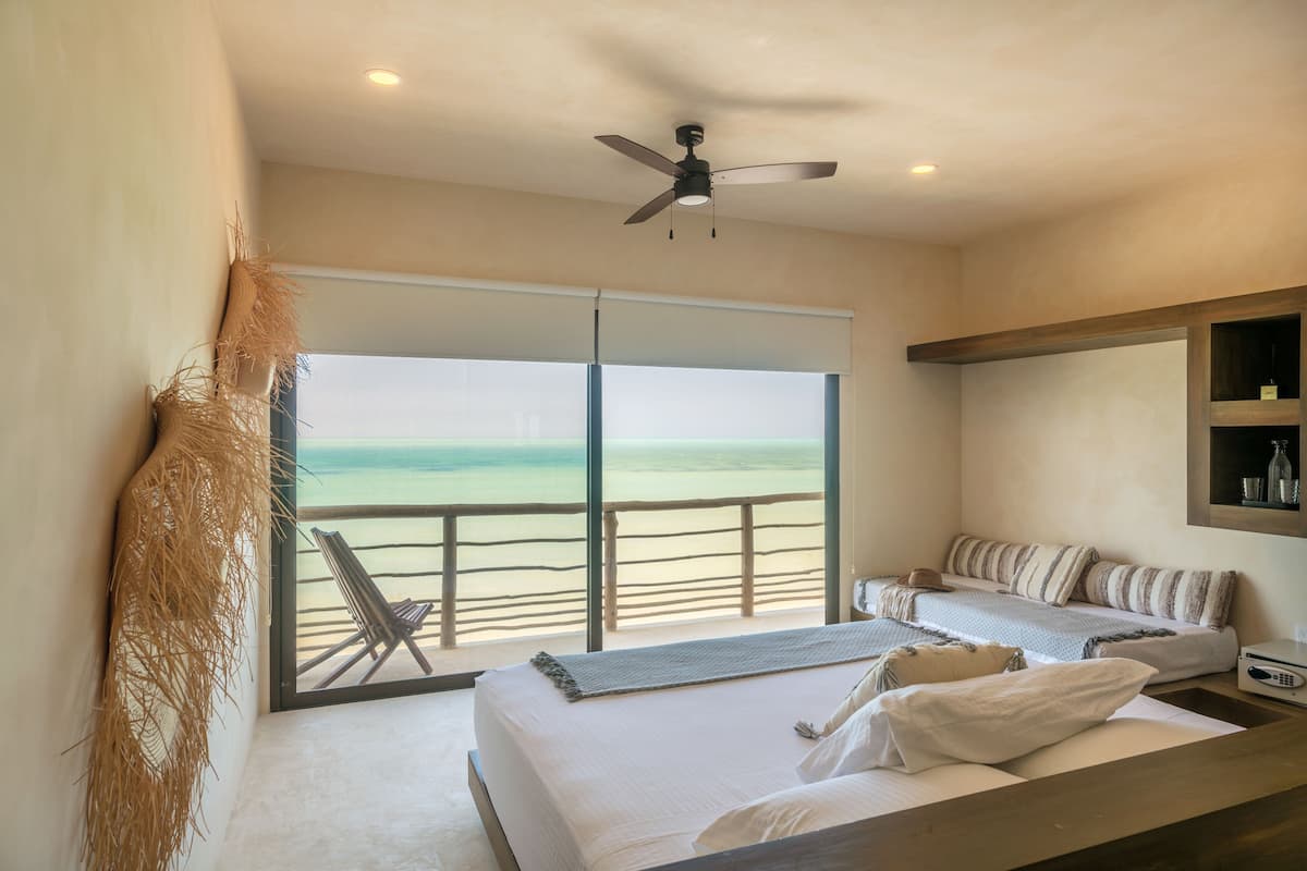 Un dormitorio con cama, mesita de noche, ventilador de techo y vista a la playa.